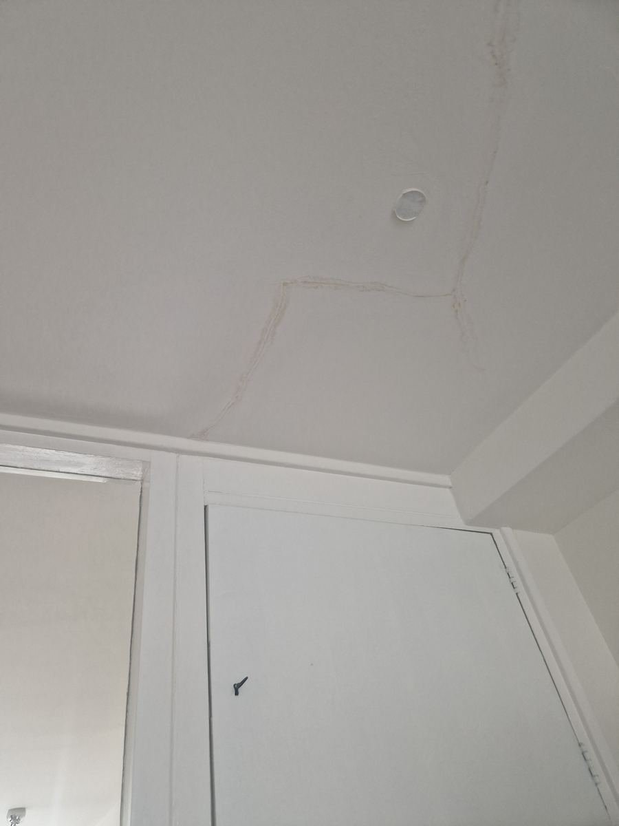 Scheur en vochtplek in een plafond naast een kozijn