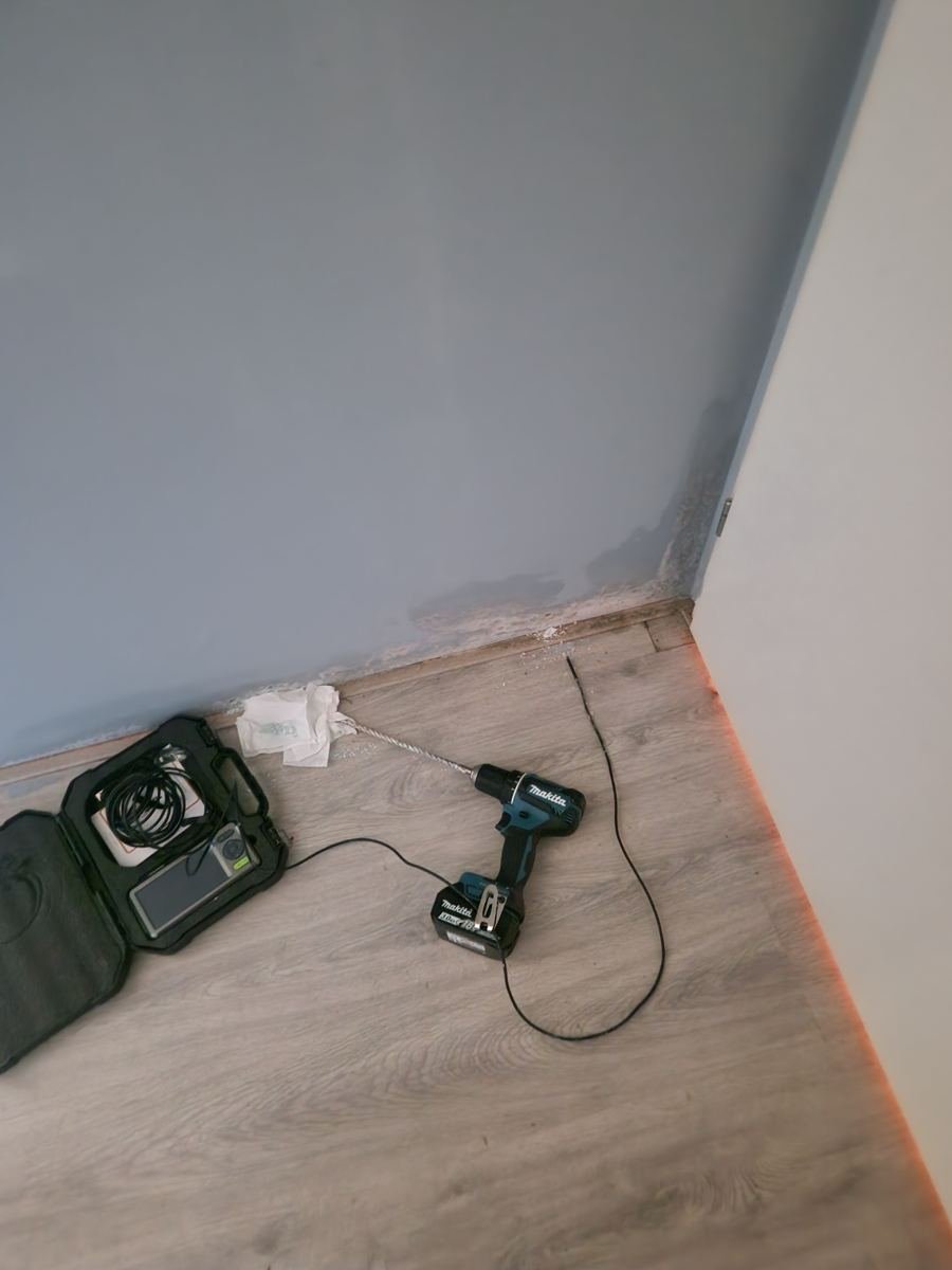 Boor en meetapparatuur op de vloer bij een muur met vochtschade
