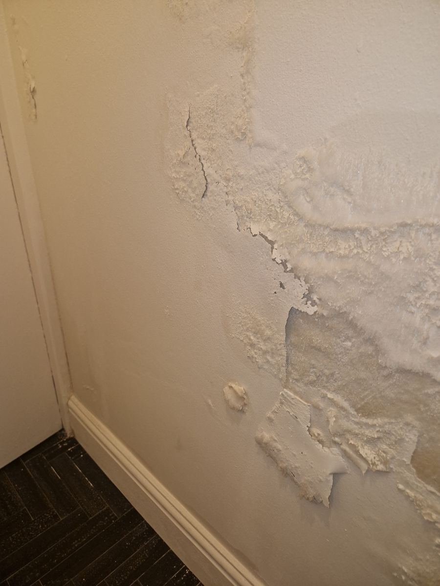 Loslatend pleisterwerk door vochtschade onderaan een muur